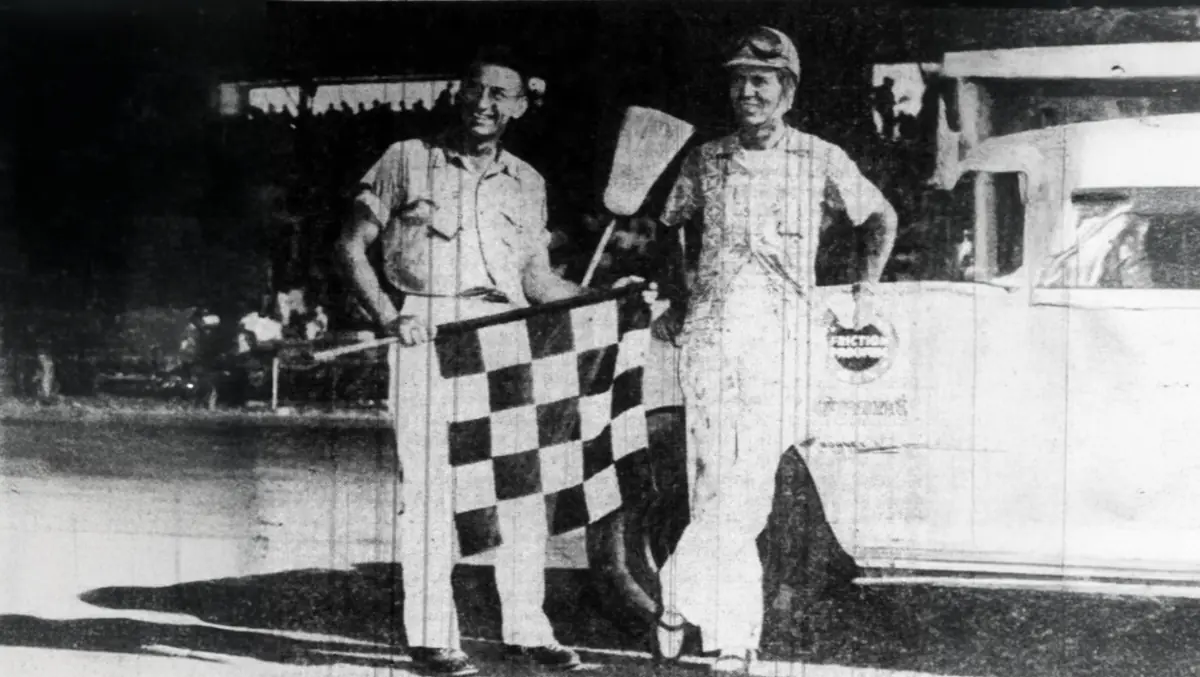 Photograph of the Tim Flock posing with the checkered flag after a race at Playland Park