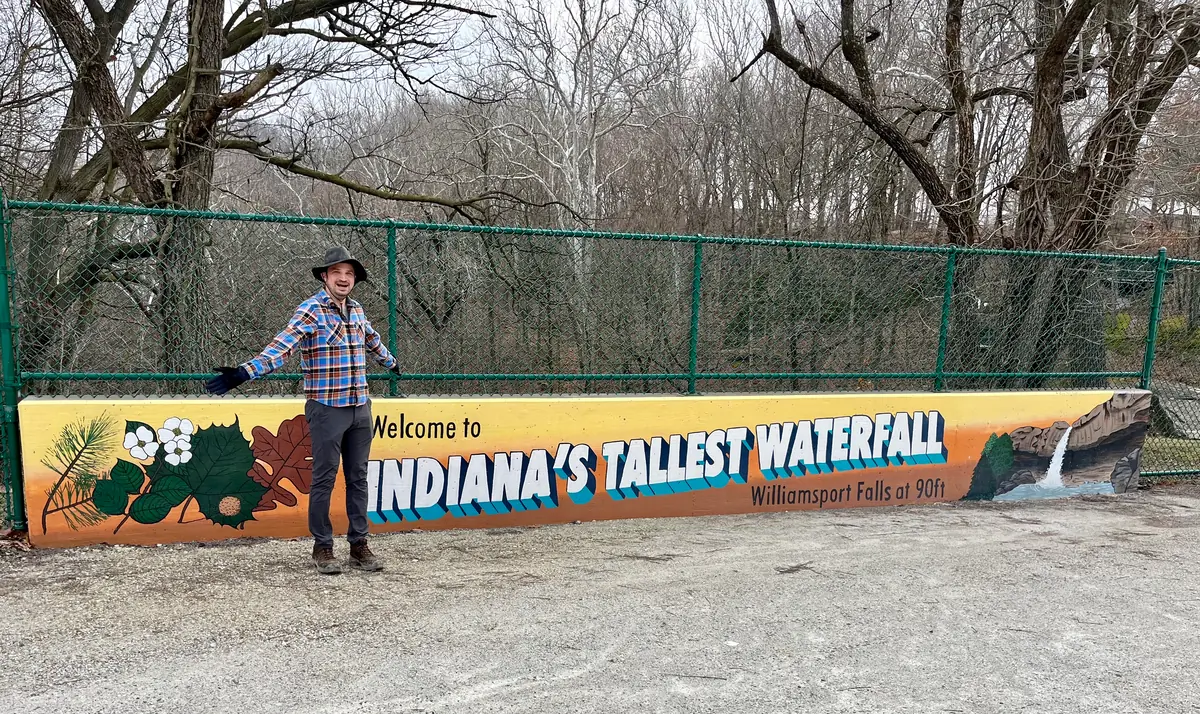 Aaron Helman stands in front of a sign advertising Williamsport Falls